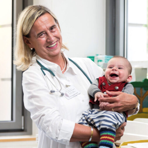 Annette Grüters-Kieslich hält ein fröhlich lachendes Baby auf dem Arm.