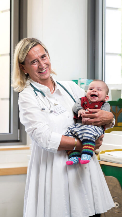 Annette Grüters-Kieslich hält ein fröhlich lachendes Baby auf dem Arm.